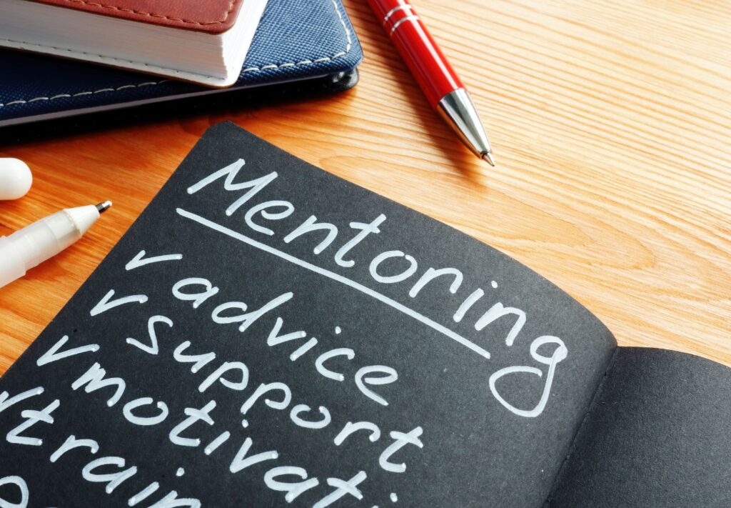 black notebook on a desk with white lettering that says "Mentoring"