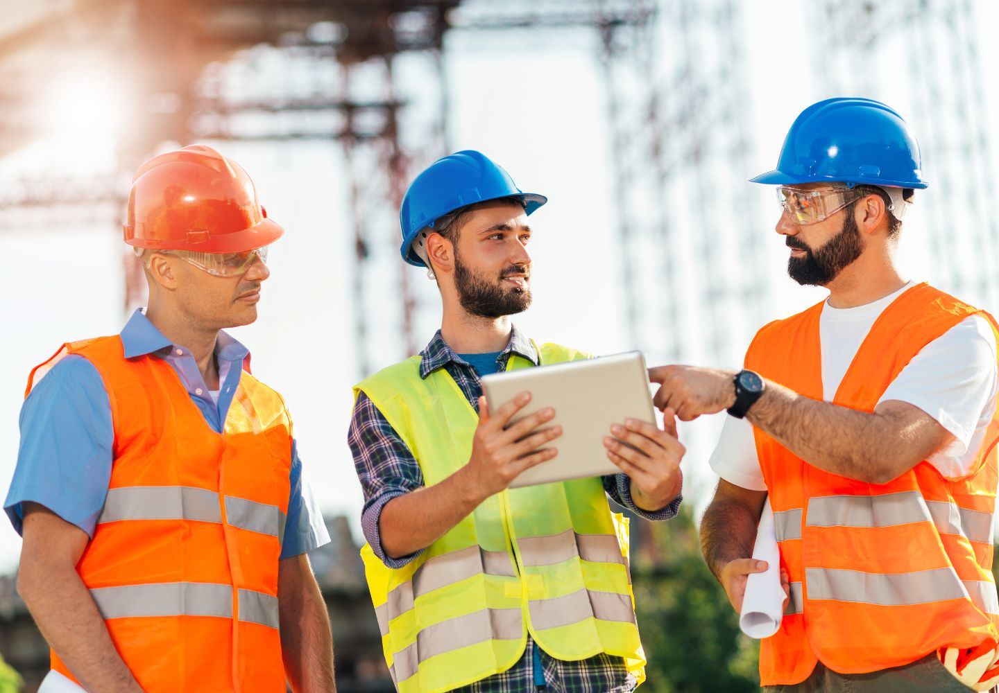 three men with hard hats looking at tablet while at construction site