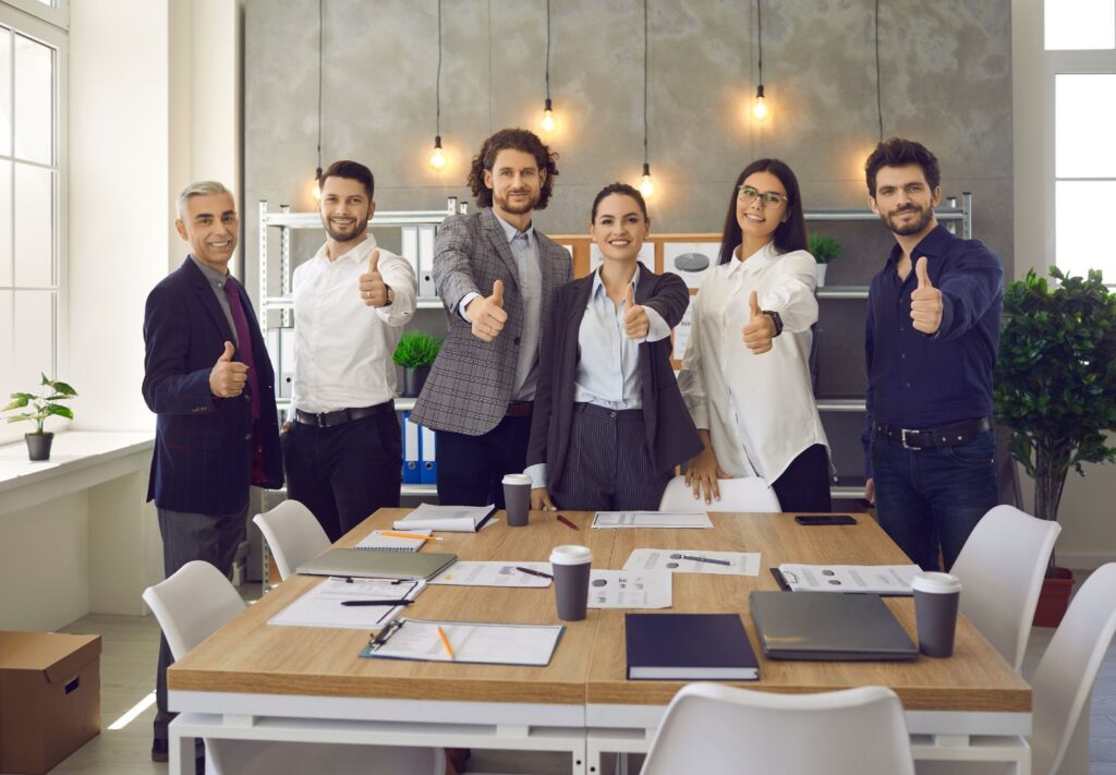 men and women standing in a conference room giving thumbs up